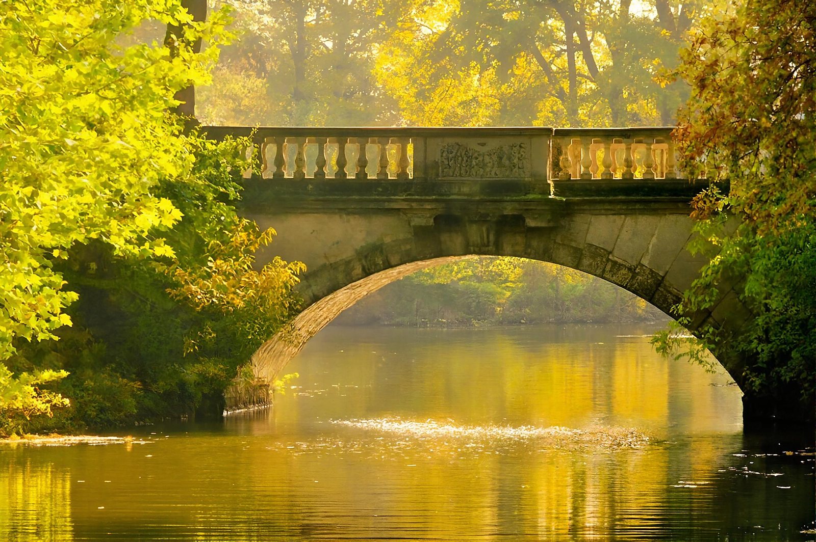 Stone bridge arching over calm water in golden autumn light
